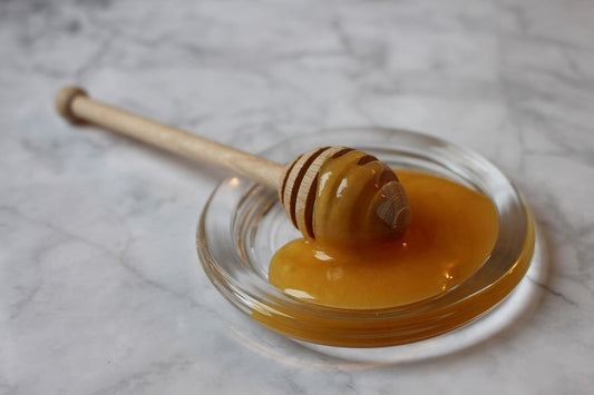 Une cuillère en bois est soigneusement posée sur un plat, couverte d'une généreuse quantité de miel doré qui déborde légèrement sur les bords.