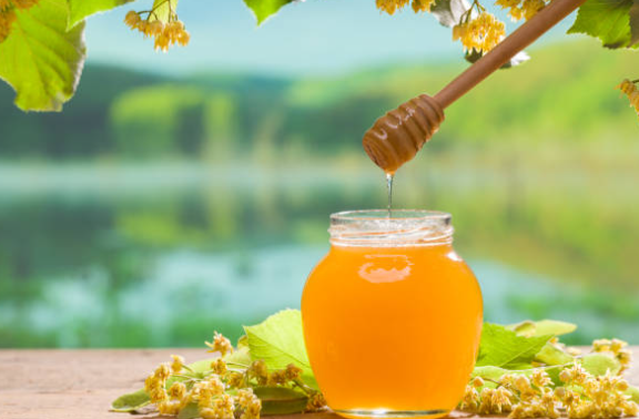 pot de miel de tilleul avec une cuillère en bois, déversant doucement le miel doré.