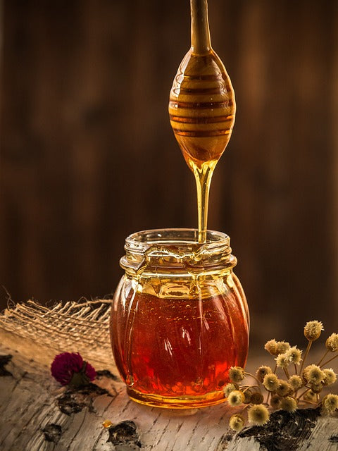 Photo d'un pot de miel de châtaignier avec une cuillère en bois, déversant doucement le miel doré.