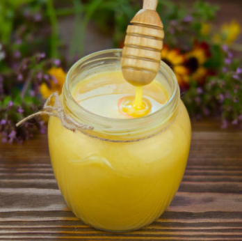 Une image d'un pot de miel contenant de la gelée royale, accompagné d'une cuillère en bois de miel.