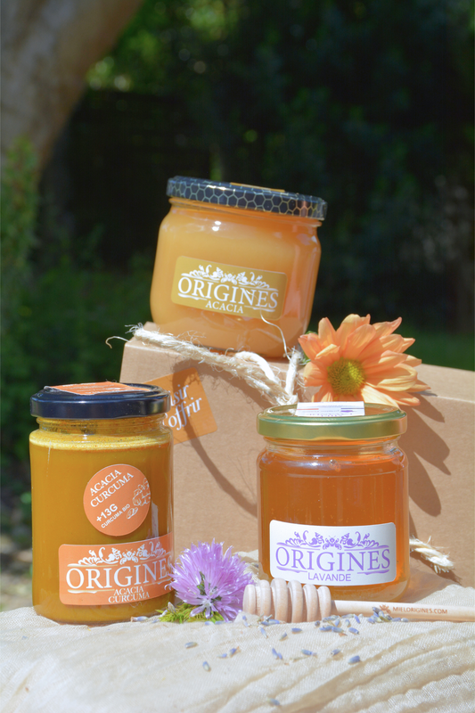 Coffret cadeau de miel mettant en valeur notre miel de tilleul, miel de lavande et miel de curcuma Origines, avec une cuillère à miel, dans un bel environnement.